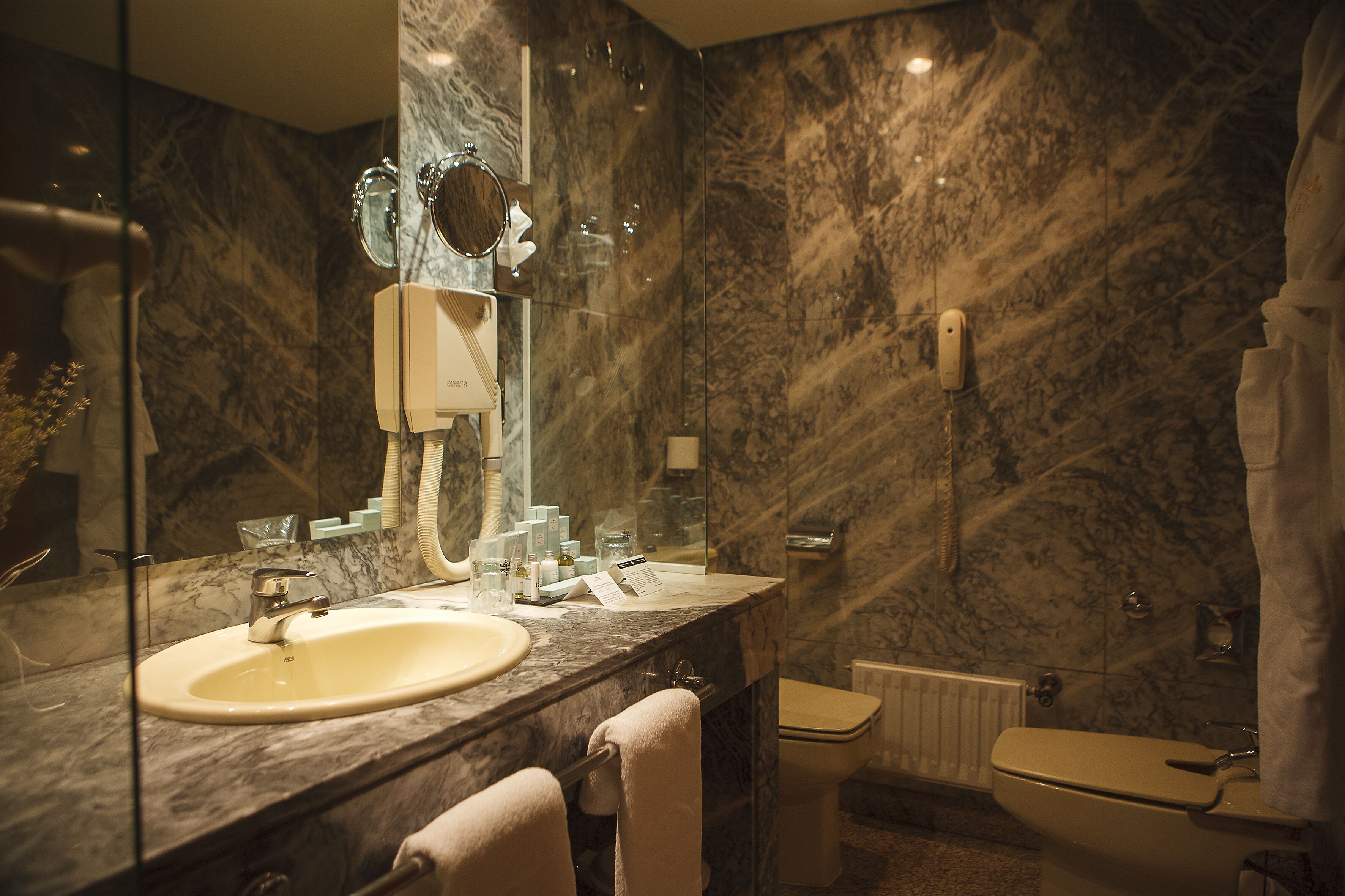 A bathroom with a marble sink, a mirror, a toilet, and a shower curtain.