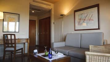 A hotel room with a sofa, a wooden desk, a chair, a coffee table with a vase, and a framed abstract painting.