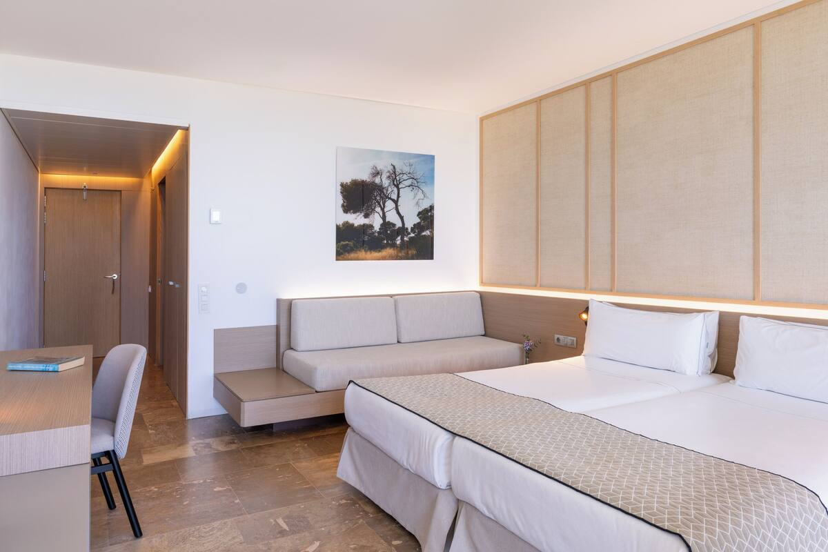 A hotel room with a bed, a sofa, a desk, and a painting on the wall.
