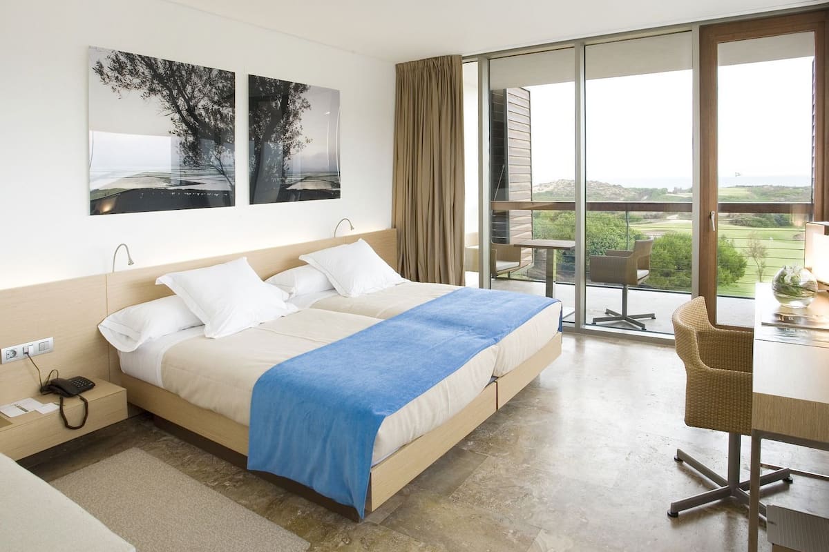 A bedroom with a bed, a desk, and a balcony with a view.