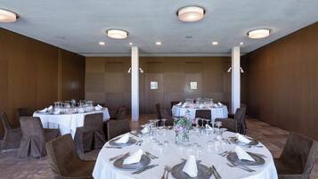 A well-lit banquet hall with round tables set for dining, featuring white tablecloths, silverware, and glassware.