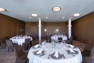 Un salón de banquetes bien iluminado con mesas redondas dispuestas para el servicio de comidas, con manteles blancos, cubertería y cristalería.