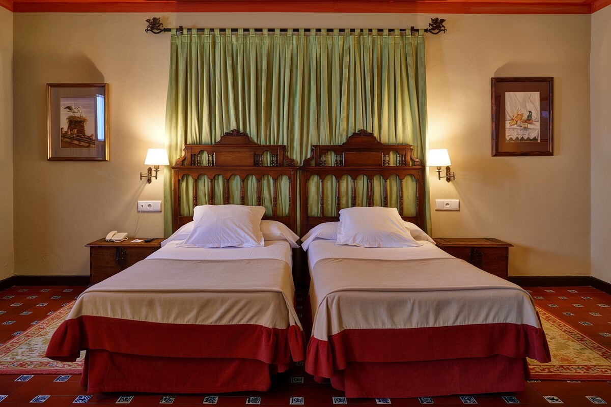 A hotel room with two beds, a green curtain, and two wall-mounted lamps.