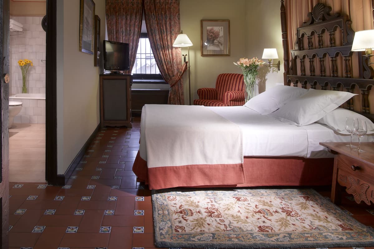 A hotel room with a bed, a television, a chair, a desk, and a window with curtains.