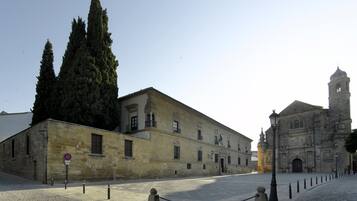 Un edificio histórico con una imponente torre campanario, un patio con adoquines y un árbol grande.
