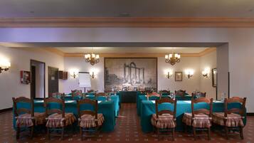 A conference room with tables and chairs, a large painting on the wall, and chandeliers.