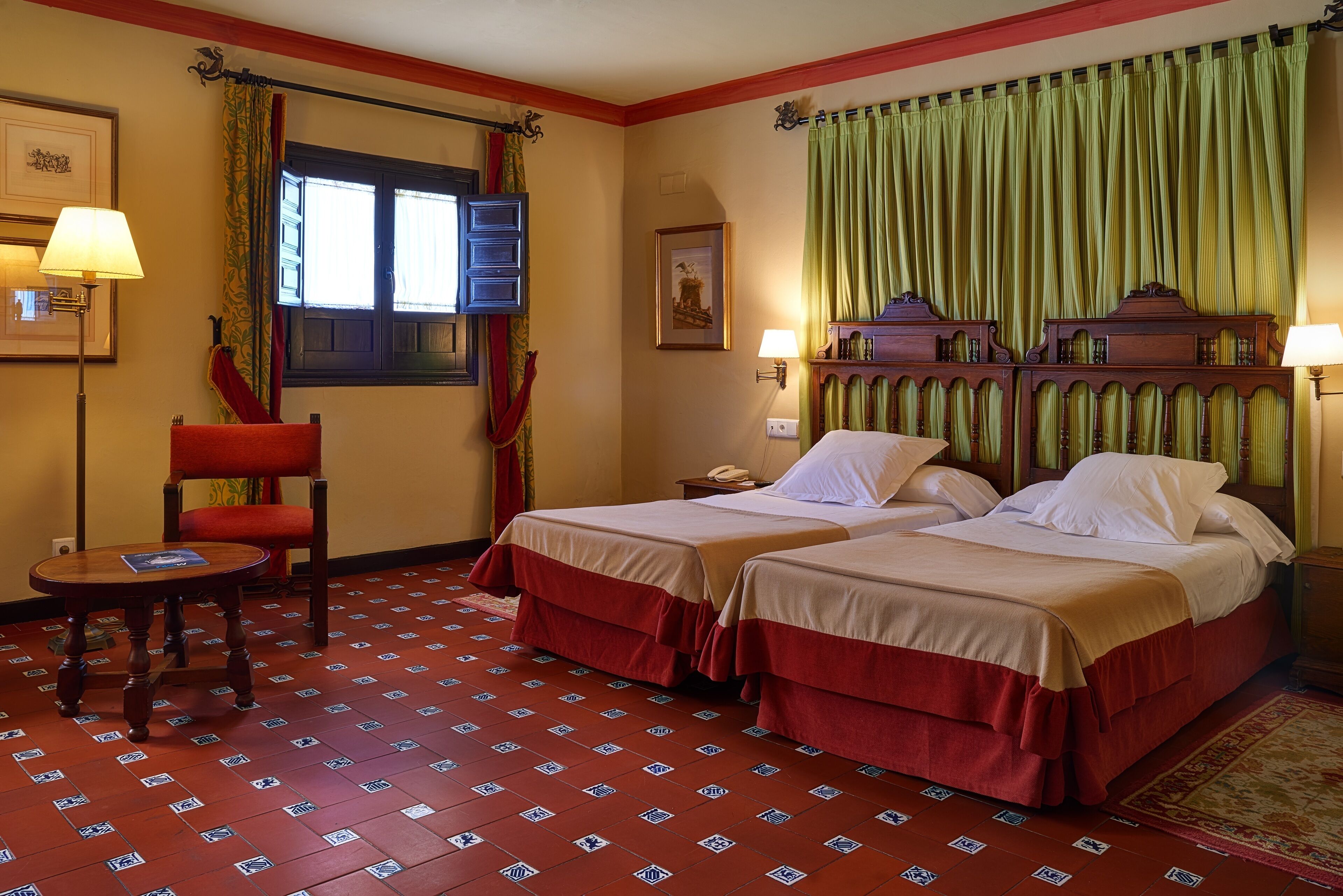 A hotel room with two beds, a chair, a small table, a nightstand, and a window with curtains.