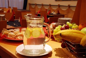 A dining table with a pitcher of lemonade, a plate of pastries, and a fruit basket. - EA Hotel Tosca (Prague)