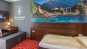 A hotel room with a bed, a TV, a desk, and a wall-mounted screen displaying a mountain landscape. - Hotel Mozart Bad Gastein (Bad Gastein)