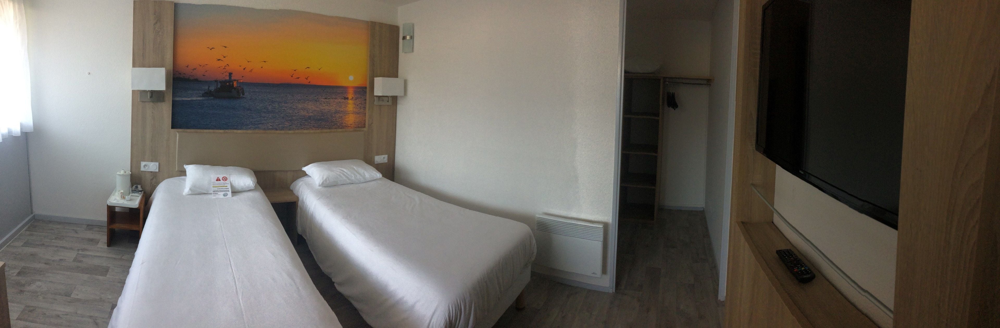 Une chambre d’hôtel avec deux lits, un tableau représentant un coucher de soleil sur l’eau, une télévision et une armoire.