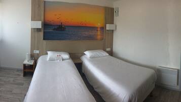 Une chambre d’hôtel avec deux lits, un tableau représentant un coucher de soleil sur l’eau, une télévision et une armoire.