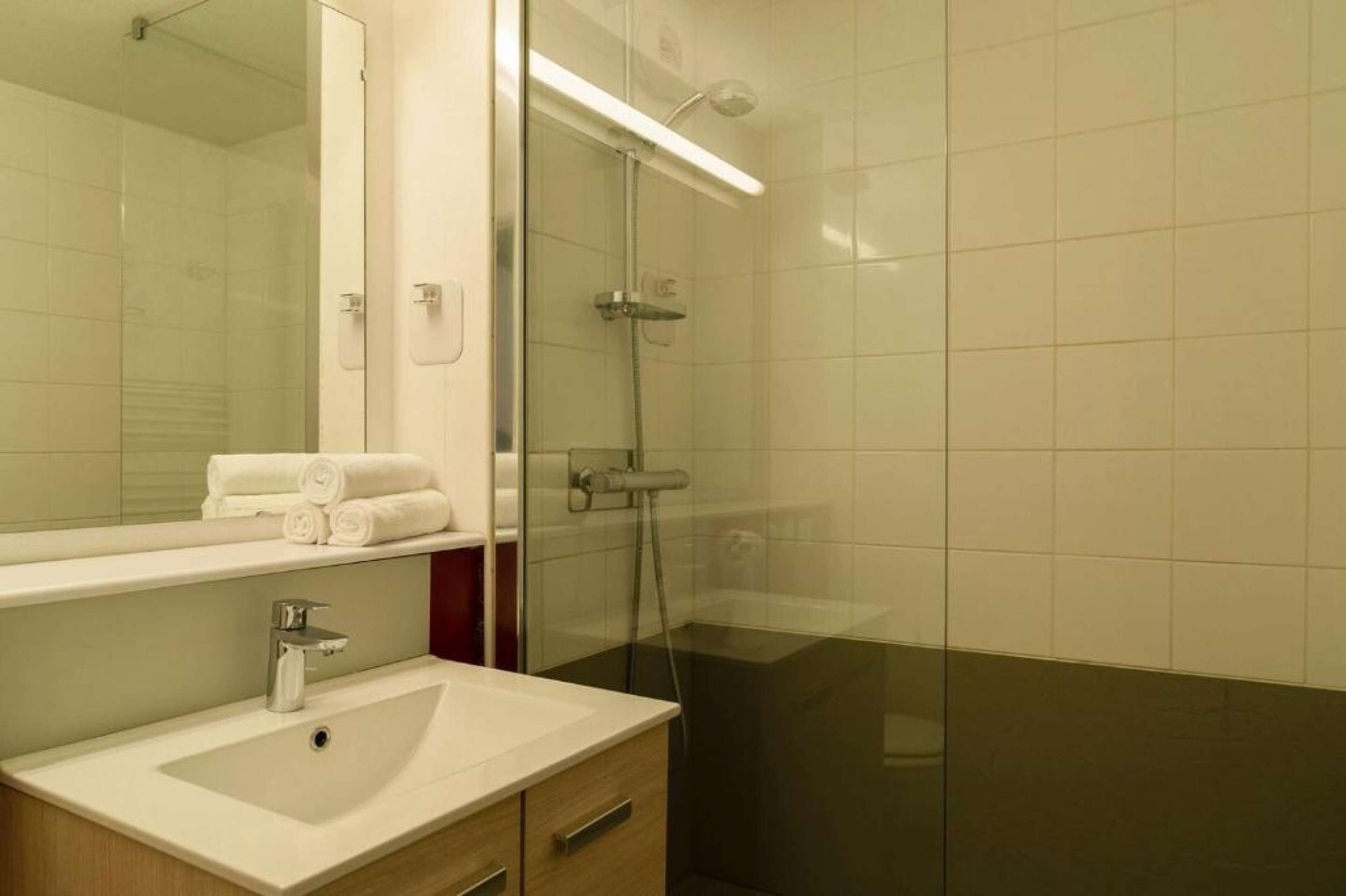 A modern bathroom with a glass shower enclosure, a sink with a mirror, and neatly folded towels on the counter.