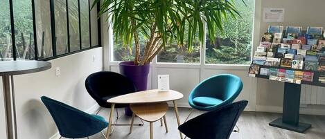 Un espacio de oficina moderno con un gran ventanal, una planta en maceta, dos sillas azules, una mesita y una exhibición de folletos.