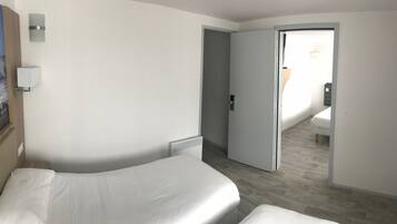 A hotel room with a bed, a nightstand, a wall-mounted light, and a door leading to another room.