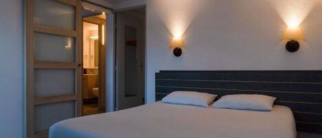 A bedroom with a bed, two wall-mounted lights, and a sliding door leading to a bathroom.