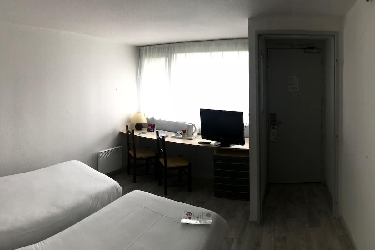 Habitación de hotel con dos camas, un escritorio con computadora y vista al mar a través de una ventana.
