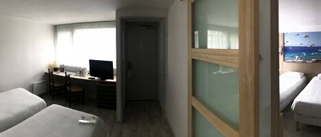 A hotel room with two beds, a desk with a computer, and a view of the sea through a window.