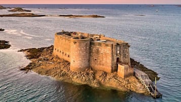 Un castillo costero con estructura fortificada, ubicado en una isla rocosa rodeada de agua.