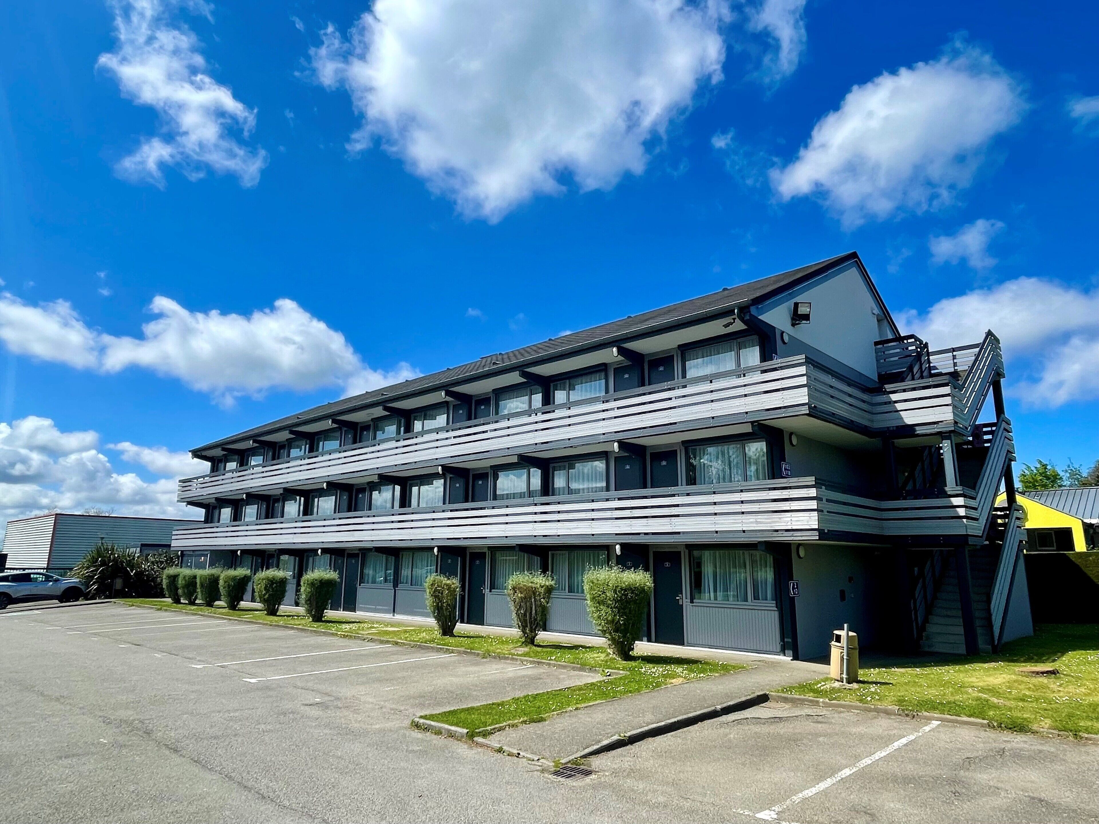 A modern multi-story hotel with a parking lot and a clear blue sky.