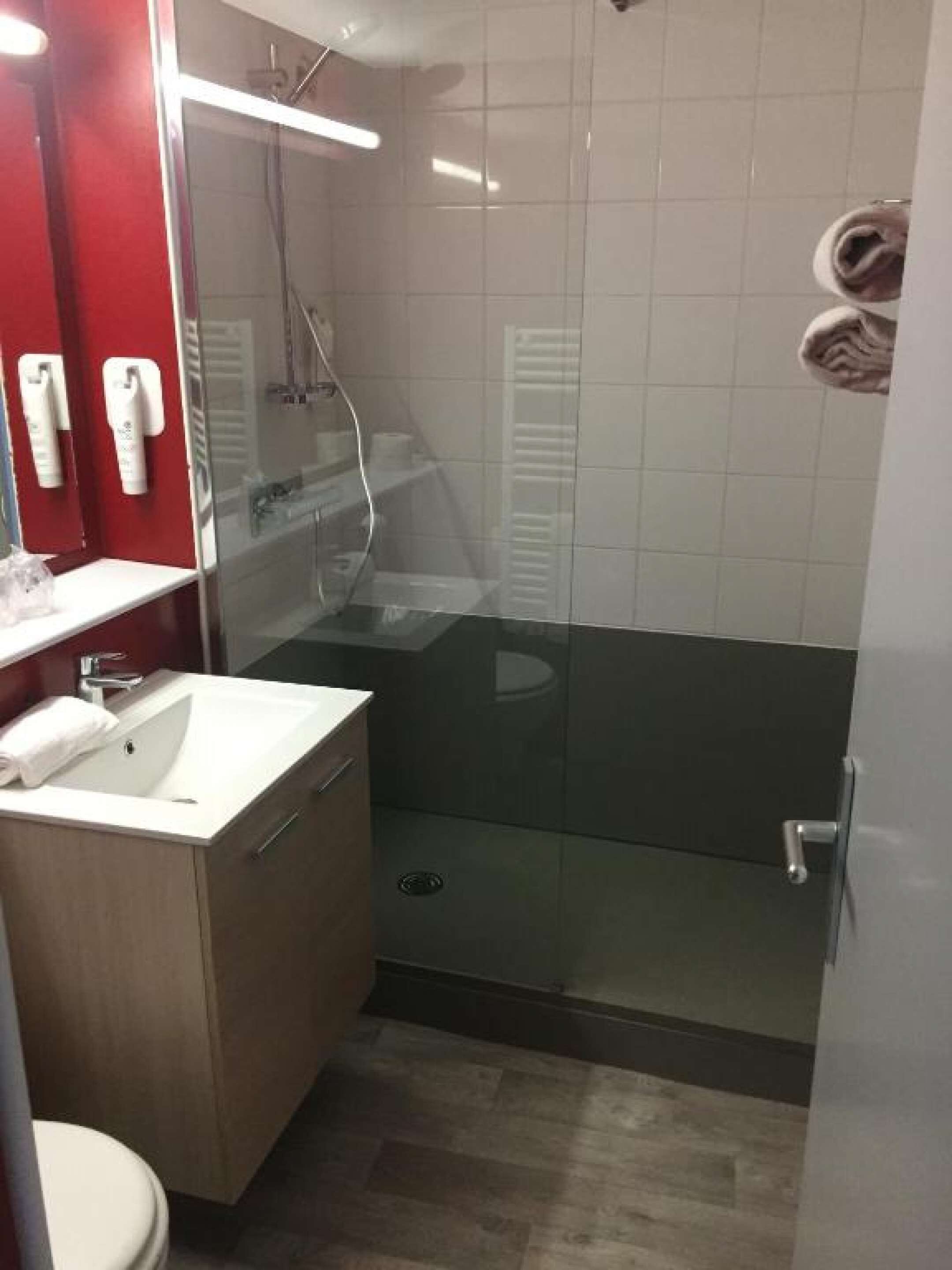 A modern bathroom with a glass-enclosed shower, a white sink, and a red accent wall.