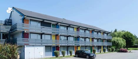 A multi-story motel with a flat roof, balconies, and a parking lot.