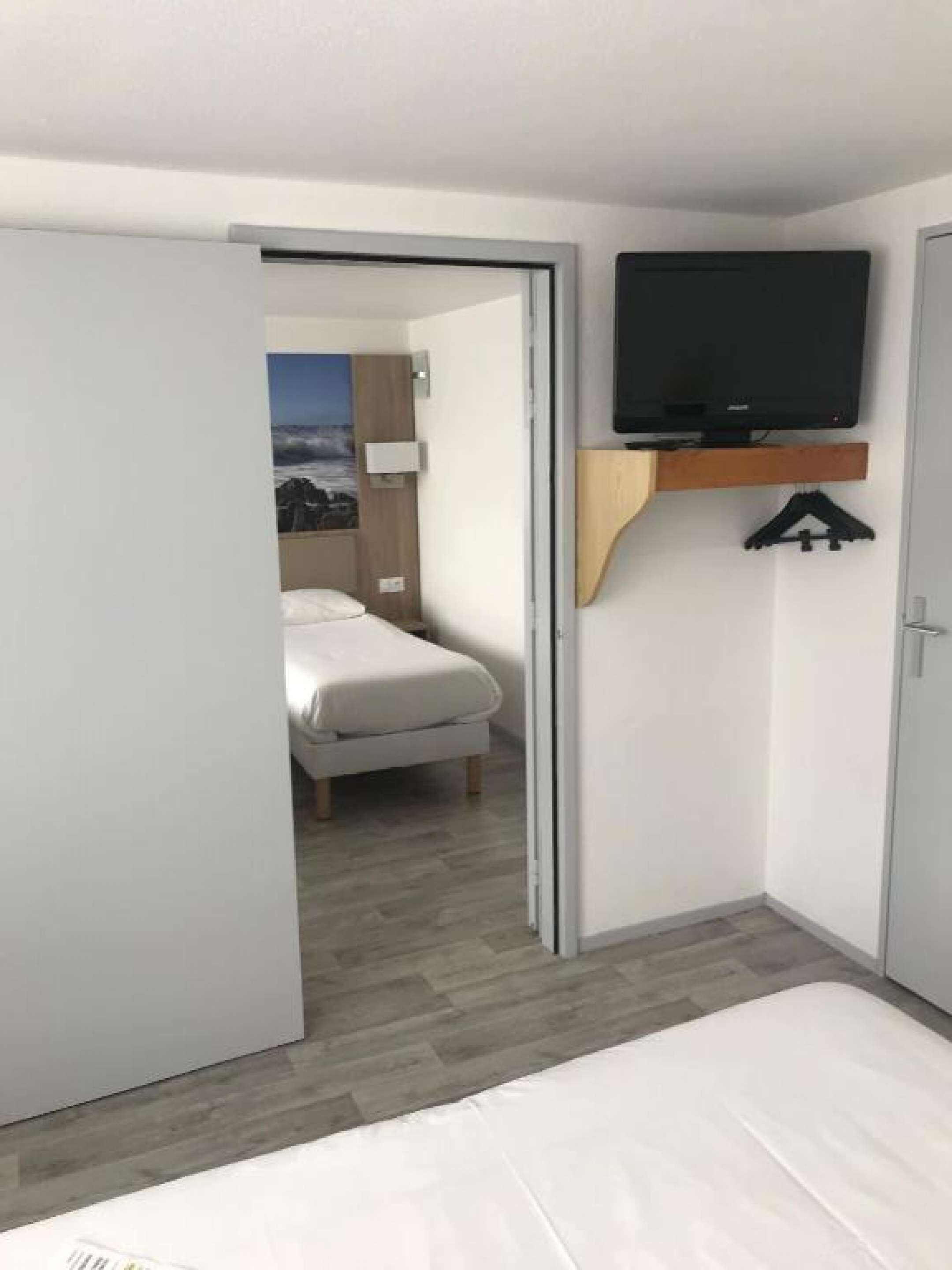 Una habitación de hotel con una cama, un televisor fijado en un estante de madera y una puerta que da a otra habitación.