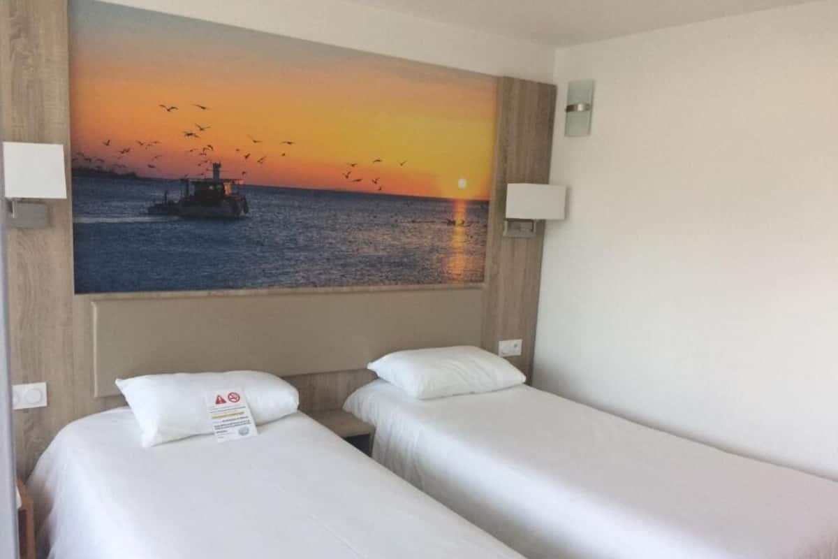 Habitación de hotel con dos camas individuales, un cuadro grande de un atardecer sobre el agua y un cabecero de madera.