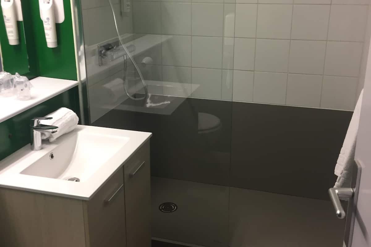 Un baño con ducha envuelta en vidrio, un lavamanos con espejo y un perchero para toallas.