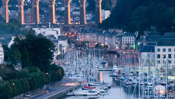 Ein Yachthafen mit zahlreichen Schiffen, eine Brücke im Hintergrund und Gebäude entlang des Ufers.