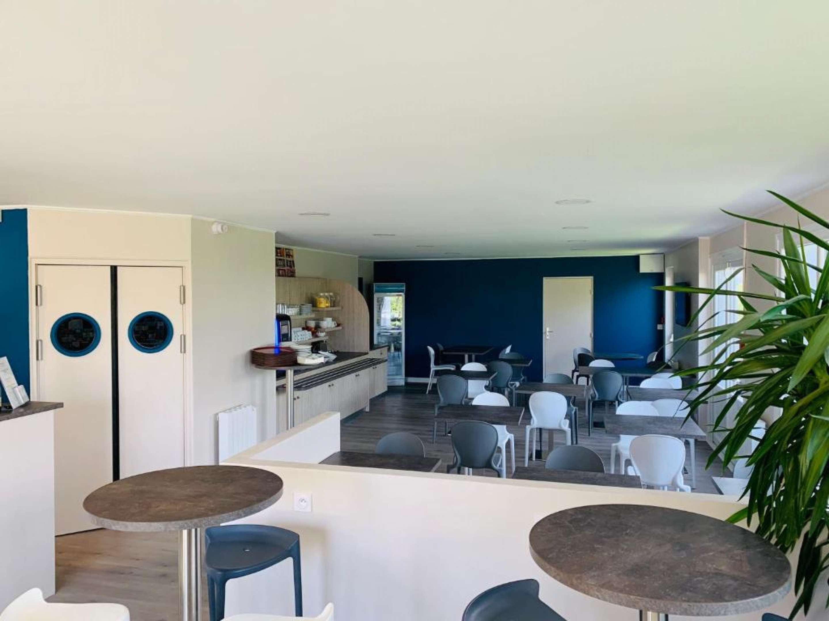 A modern dining area with round tables and chairs, a kitchen area with a counter and cabinets, and a blue accent wall.