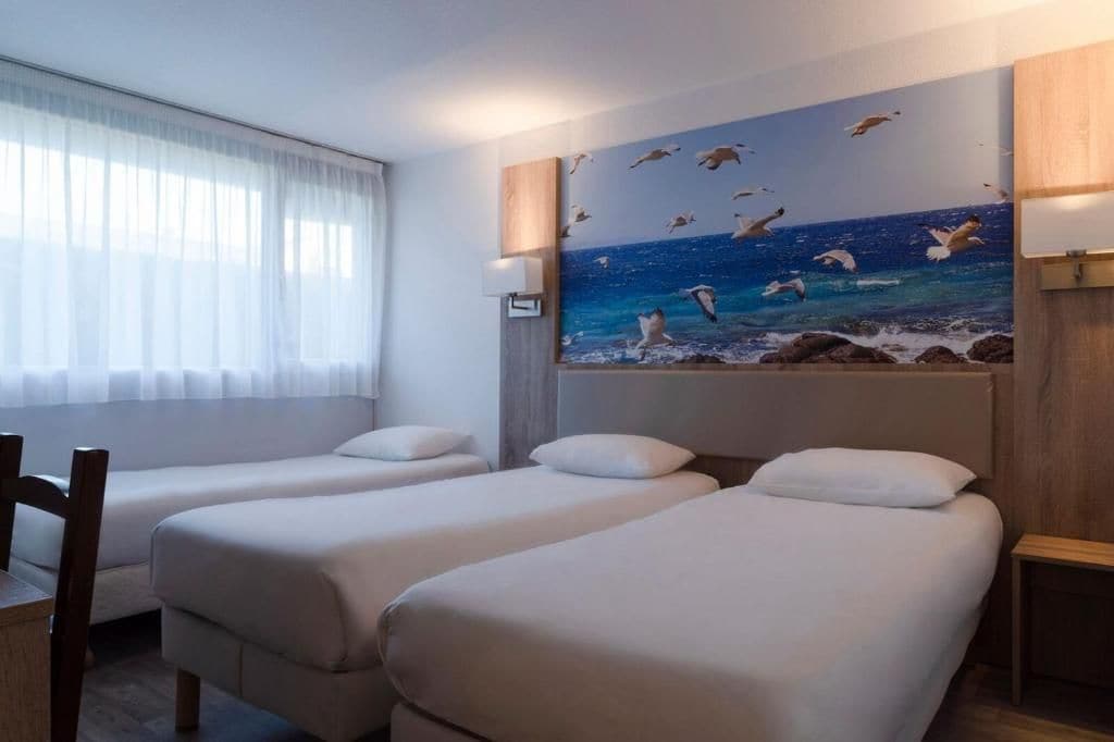 A hotel room with two beds, a window with sheer curtains, and a wall mural of seagulls.