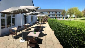 Eine Terrasse im Freien mit Tischen, Stühlen und Sonnenschirmen, sowie ein Gebäude im Hintergrund.