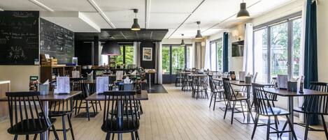 Un café amplio con suelo de madera, sillas y mesas negras. Hay un menú en una pizarra en la pared y un ventanal que proporciona luz natural.