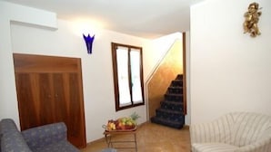 A living room with a sofa, a small table with fruit, a chair, a wooden door, and a staircase. - Cà dei Leoni (Venice)
