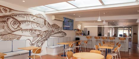Um restaurante com um mural de peixes, mesas, cadeiras e um espaço de bar.