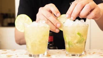Two glasses of a yellow beverage with ice and lime slices, held by a person.