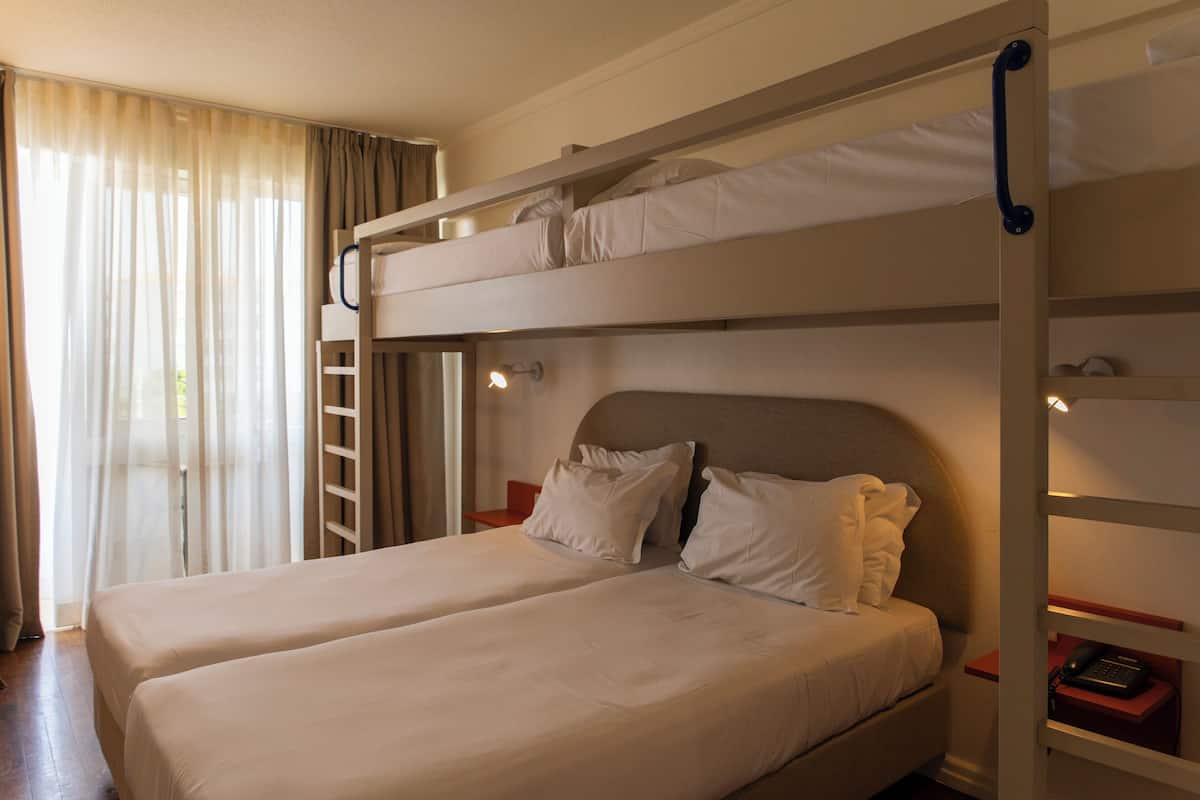 A bunk bed room with two beds, a ladder, a bedside table with a phone, and a window with curtains.
