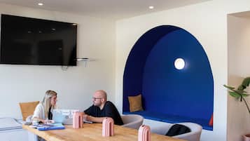 A modern meeting room with a wooden table, two cushioned chairs, a large blue arched wall, and a mounted television.