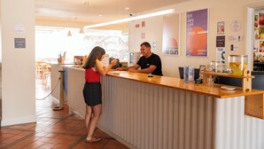 A reception area with a wooden counter, a woman and a man standing behind it, and various amenities like a coffee machine and glassware. - WOT Lagos Montemar Soul (Lagos)