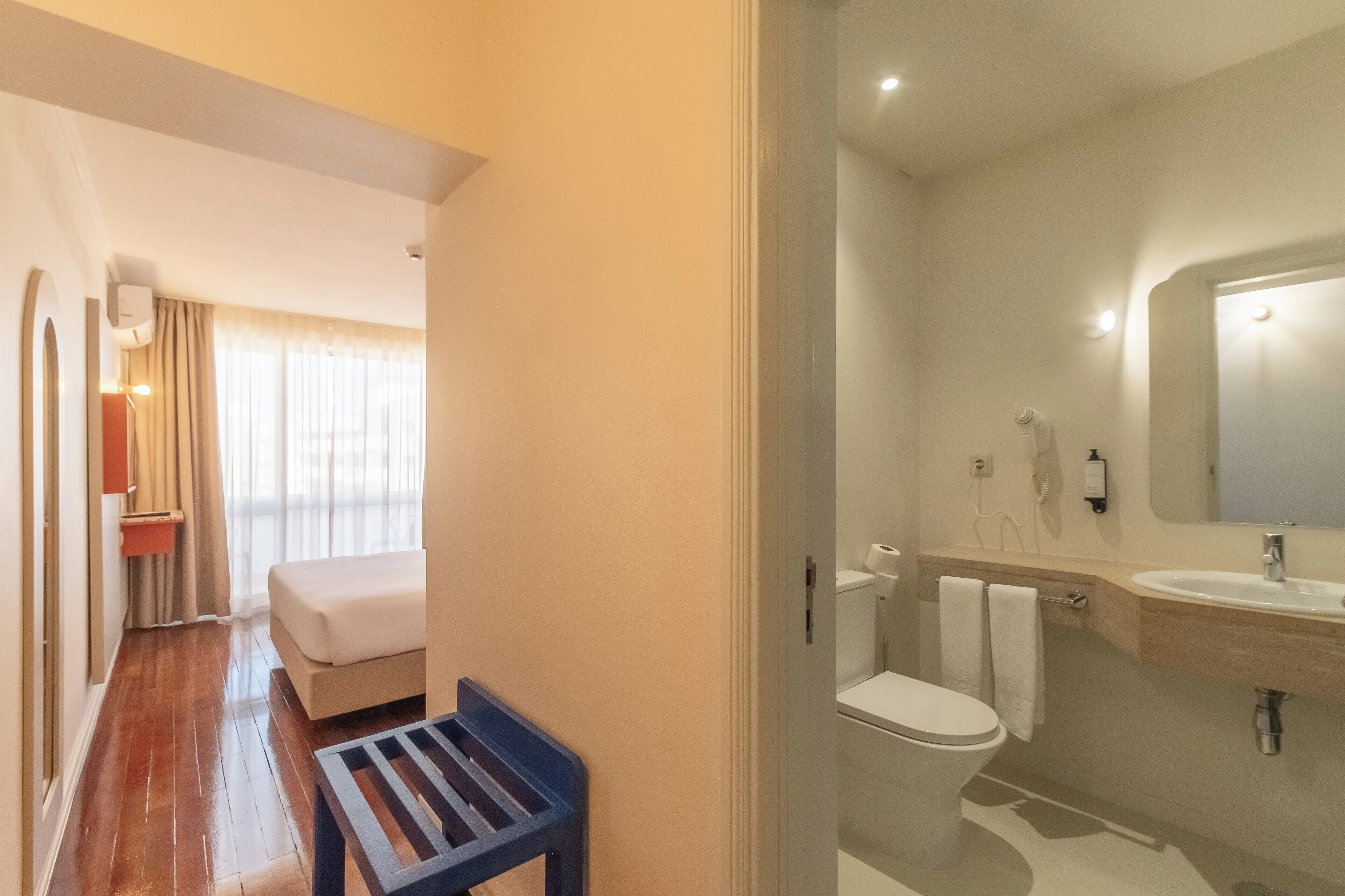 Ein Hotelzimmer mit einem Bett, einer Sitzbank, einem Badezimmer mit Waschbecken und Toilette.