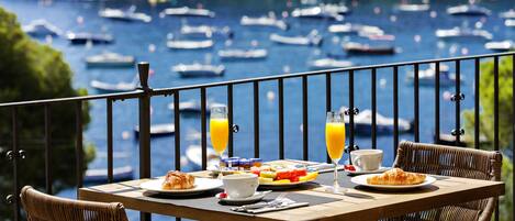 Mesa de comedor con alimentos para el desayuno y bebidas, con vista a un puerto deportivo con barcos.