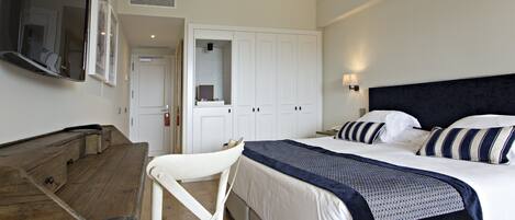 A bedroom with a bed, a desk, and a chair. There is a wardrobe and a television mounted on the wall.
