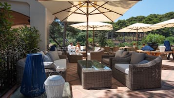 An outdoor patio with wicker furniture, large umbrellas, and potted plants.
