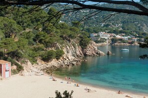 A coastal beach with clear turquoise water, a sandy shore, and a small building on the left. - Hotel Aiguablava (Begur)