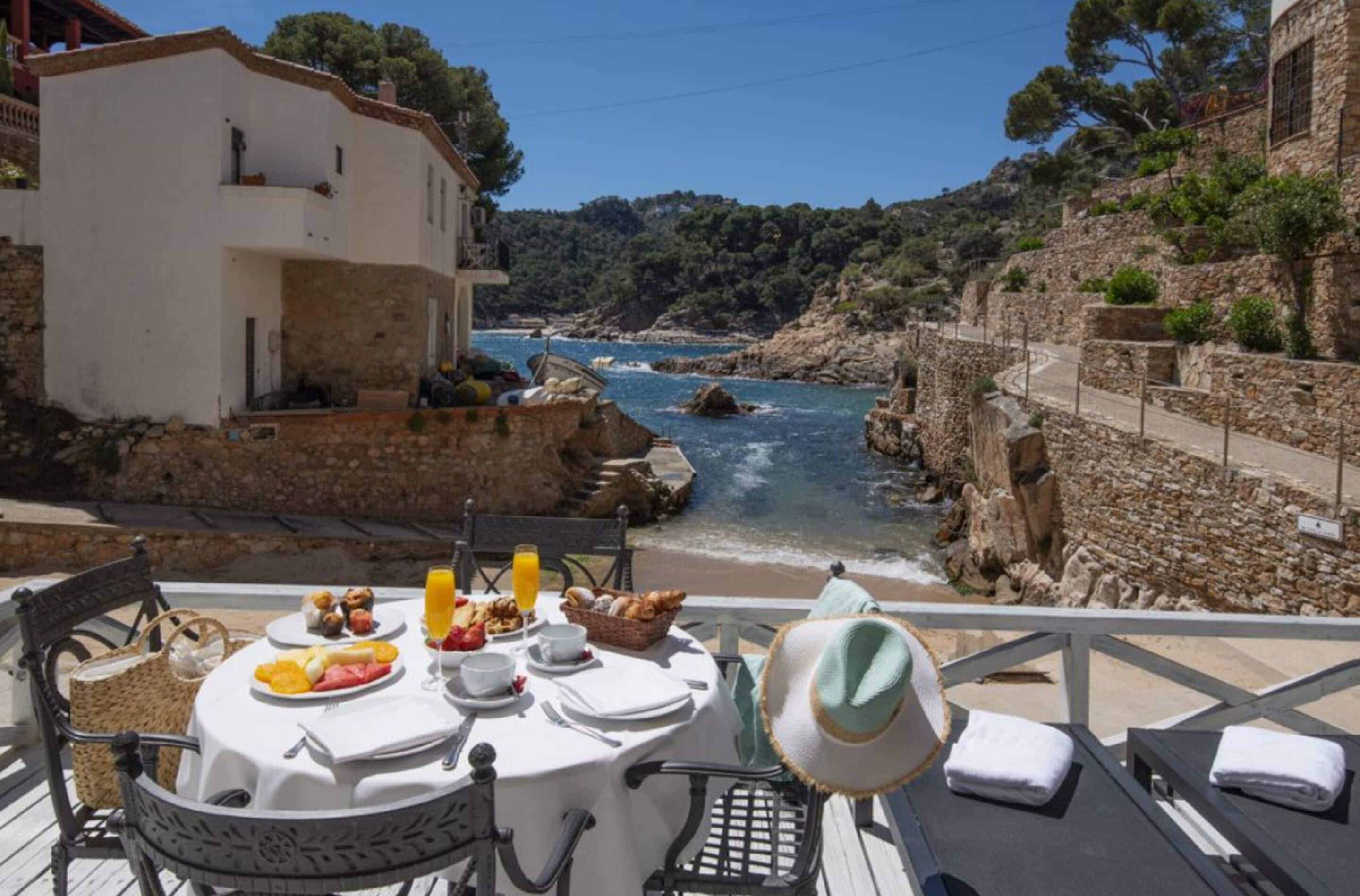 Una mesa lista para el desayuno, con vistas a un litoral rocoso y un río.