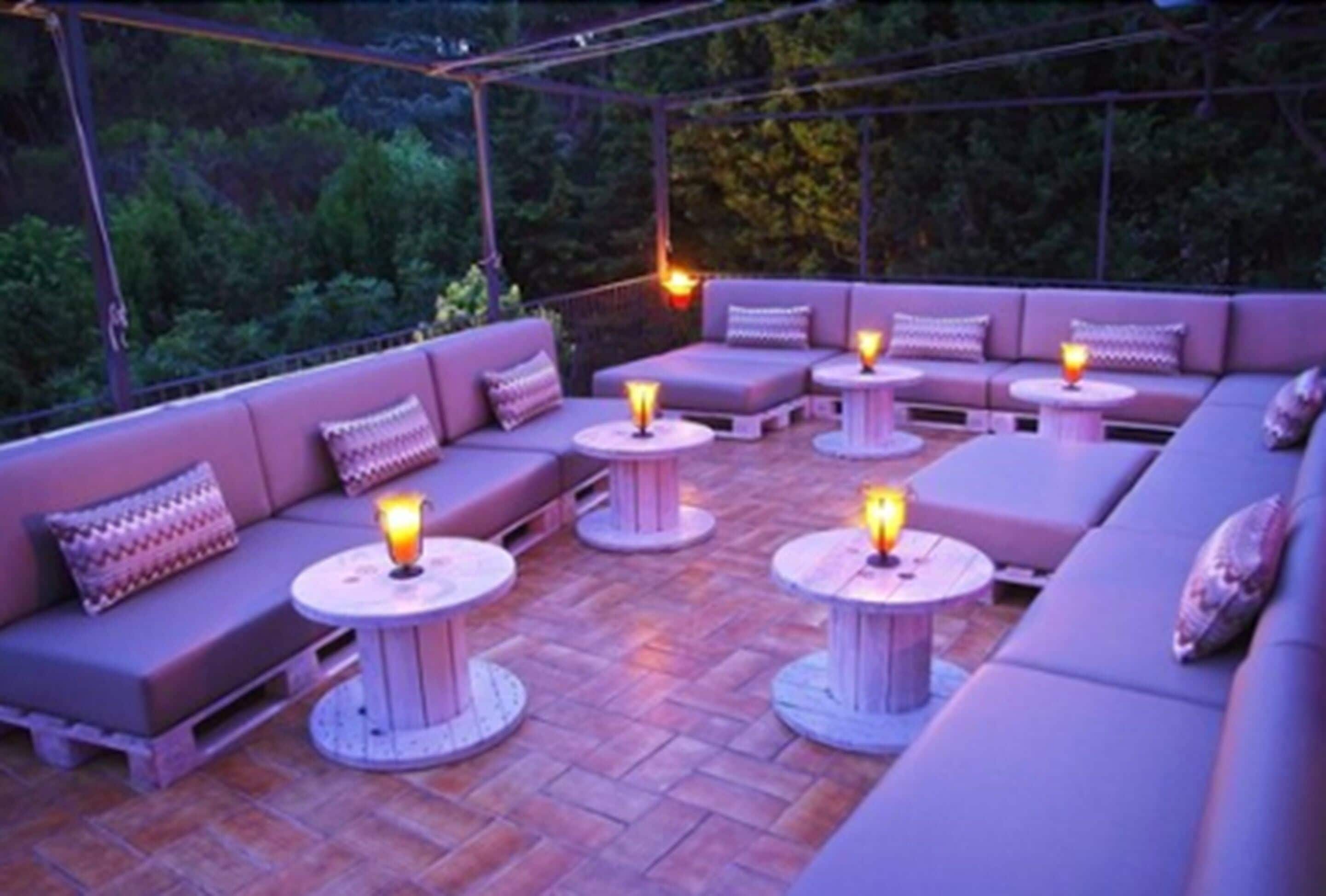 An outdoor seating area with cushioned sofas and round tables, each with a candle.
