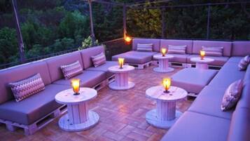 An outdoor seating area with cushioned sofas and round tables, each with a candle.