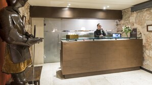A reception desk with a receptionist, a stone wall, and a knight statue. - Parador de Alarcón (Alarcon)