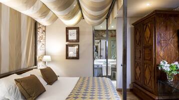 A hotel room with a large bed, a wooden wardrobe, a bathroom with a mirror, and a window with curtains.