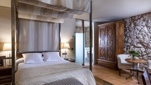 A bedroom with a canopy bed, a stone wall, a wooden wardrobe, a bedside table, and a chair with a table. - Parador de Alarcón (Alarcon)